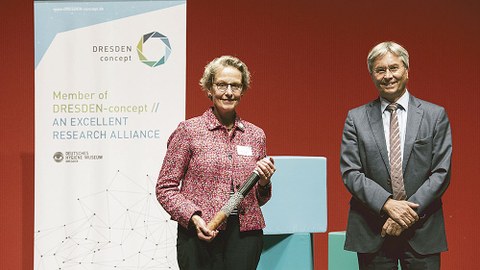 Prof. Ursula M. Staudinger hält den DRESDEN-concept-Staffelstab, den sie von ihrem Vorgänger Prof. Hans Müller-Steinhagen übergeben bekommen hat, in der Hand.
