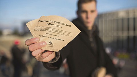 Mann hält Kaffeefilter mit Aufschrift "Community kann Kontext. Filter nicht." in der Hand.