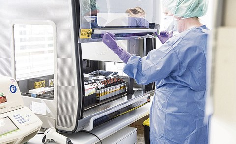 Eine Person in Laborkittel mit Mundschutz öffnet einen Laborschrank.
