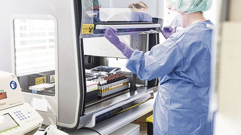 Eine Person in Laborkittel mit Mundschutz öffnet einen Laborschrank.