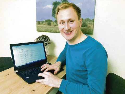 Erik Bartzsch sitzt am Schreibtisch vor einem Laptop und schaut lächelnd in die Kamera.