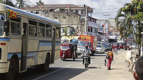 Straßenszene in Sri Lanka mit Lastwagen, Autos, Motorrädern und Fußgängern.
