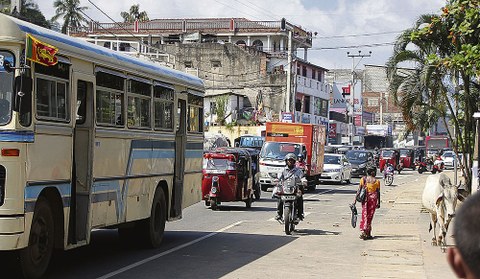 Straßenszene in Sri Lanka mit Lastwagen, Autos, Motorrädern und Fußgängern.