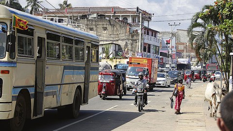 Straßenszene in Sri Lanka mit Lastwagen, Autos, Motorrädern und Fußgängern.