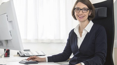 Prof. Roswitha Böhm sitzt am Schreibtisch und lächelt in die Kamera.