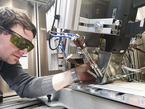 Techniker Erik Findeisen positioniert Thermoelemente an einem Laserkopf im Laserlabor des Instituts für Energietechnik an der TU Dresden. Darunter ist eine lackierte Probe zu sehen, die den Schutzanstrichen in alten Kernkraftwerken ähnelt.