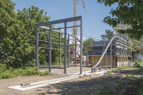 Die Stahl-Glas-Konstruktion steht auf dem Baugrundstück. Im Hintergrund rechts steht die zweisöckige BOX.