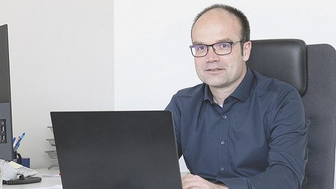 Prof. Lars Bernard sitzt am Schreibtisch. Vor ihm steht ein aufgeklapptes Laptop, auf dem er tippt. Prof. Bernard sieht den Betrachter an.