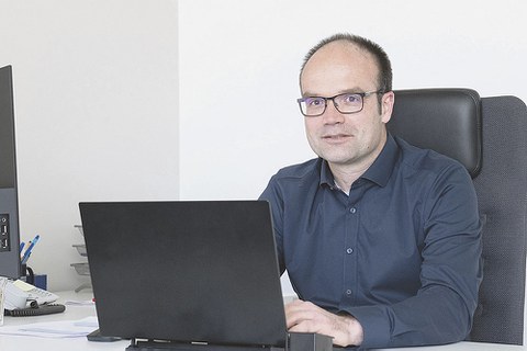 Prof. Lars Bernard sitzt am Schreibtisch. Vor ihm steht ein aufgeklapptes Laptop, auf dem er tippt. Prof. Bernard sieht den Betrachter an.