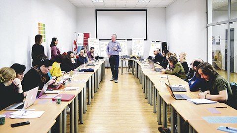 Christian Gerhardts referiert vor Interessierten, die an zwei Tischreihen sitzen.