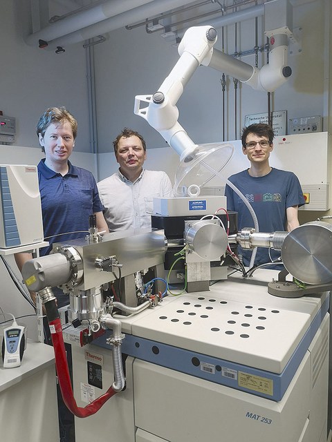 Stephan Beil, Björn Günther und Patrick Wordell-Dietrich stehen an einem Isotopen-Massenspektrometer mit Blick zum Betrachter.