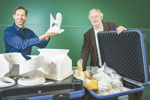 Daniel Lordick und Roland Seifert stehen hinter einem Tisch, auf dem die Modelle aufgebaut sind. Daniel Lordick hält eines in der Hand. Roland Seifert hält den Deckel des Transportkastens offen.