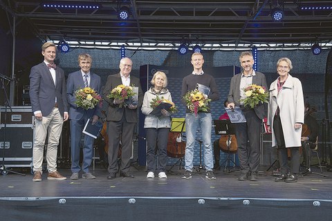 Die Ausgezeichneten stehen nebeneinander auf der Bühne und halten Blumen in der Hand.