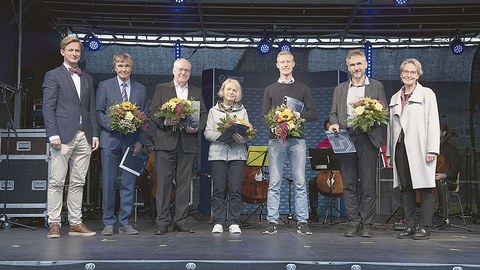 Die Ausgezeichneten stehen nebeneinander auf der Bühne und halten Blumen in der Hand.