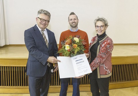 Dr. Jens Bornschein hält einen Blumenstrauß in der Hand. Links neben ihm steht Rektorin Prof. Ursula M. Staudinger, links Burkhard von der Osten. Beide halten die Urkunde in Richtung Betrachter.