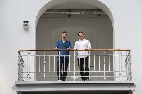 Die Schaufler-Lab-Künstler Christian Kosmas Mayer und Anton Ginzburg stehen an einer Balkonbrüstung in der Altana-Galerie. Sie schauen nach unten.