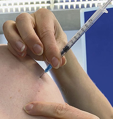 Man sieht eine menschliche Schulter, in die eine Impfspritze eingeführt wird.