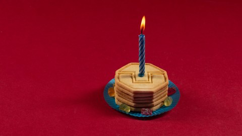 Foto von einen Keksturm auf blauem Papteller, mit einer leuchtenden Kerze. 6 Gummibären liegen im Kreis auf dem Papteller.