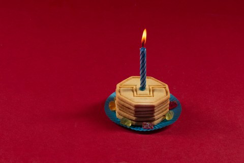 Foto von einen Keksturm auf blauem Papteller, mit einer leuchtenden Kerze. 6 Gummibären liegen im Kreis auf dem Papteller.