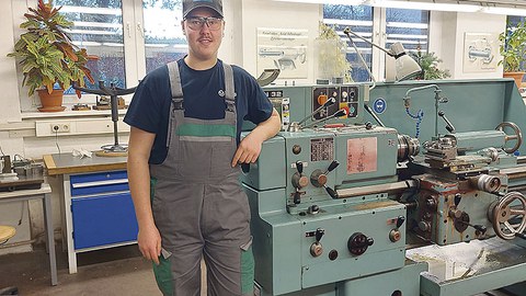 Nick Neubert steht neben einer Maschine in der Werkstatt.