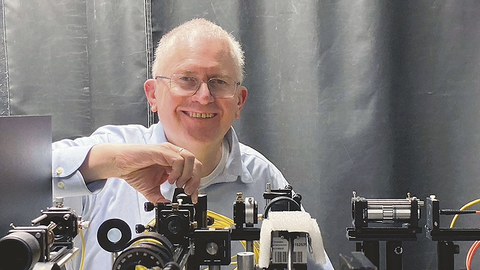 Prof. Czarske steht hinter einem Versuchsaufbau für Laserstrahlen.