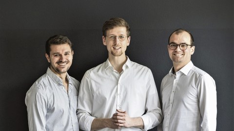 Die SpeechMind-Gründer stehen nebeneinander vor einem dunklen Hintergrund. Alle drei tragen ein weißes Hemd.