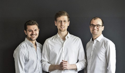 Die SpeechMind-Gründer stehen nebeneinander vor einem dunklen Hintergrund. Alle drei tragen ein weißes Hemd.