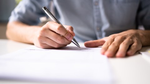 Das Foto zeigt eine Person mit einem Kugelschreiber in der Hand, die etwas unterschreibt.