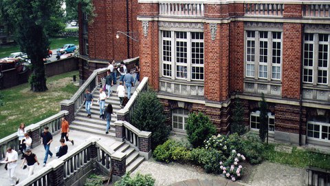 erhöhte Aufnahme von der Rückseite des Beyer-Baus mit kunstornamenten Ornamenten an der Backsteinwand und der Außentreppe, über die Studierende gehen.