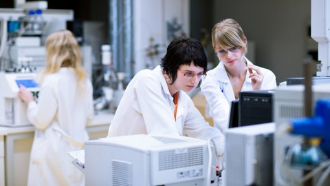 Frauen in Forschungskitteln an technischen Apparaturen