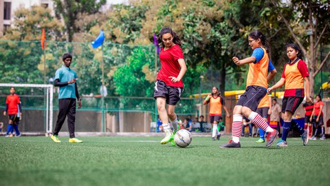 Drei Frauen spielen Fußball und im Hintergrund ist ein Schiedsrichter.
