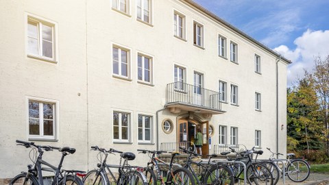 Das Foto zeigt den Eingang eines Verwaltungsgebäudes der TU Dresden auf der Nöthnitzer Straße. Vor dem Gebäude erkennt man Fahrräder an Fahrradständern. 