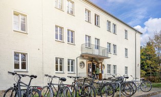 Das Foto zeigt den Eingang eines Verwaltungsgebäudes der TU Dresden auf der Nöthnitzer Straße. Vor dem Gebäude erkennt man Fahrräder an Fahrradständern. 