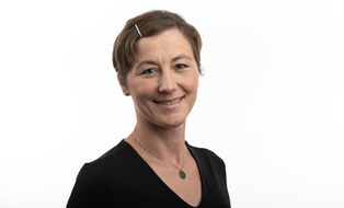 Portrait von Uta Holtzhausen - eine verschmitzt lächelnde Frau mit einer glitzernden Spange im Bob.