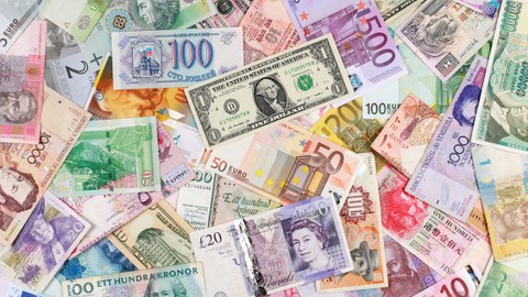 Das Foto zeigt Geldscheine aus verschiedenen Ländern mit verschiedenen Währungen. Die Geldscheine liegen verstreut übereinander.