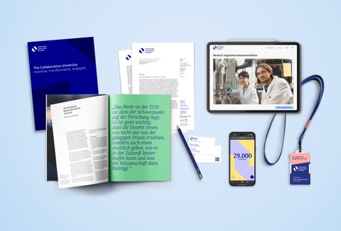 Mehrere Branding-Elemente der TU Dresden, darunter ein dunkelblaues Heft mit weißem Text, ein offenes Magazin mit grünem und weißem Text, ein Briefbogen, ein Stift, ein Smartphone mit der Zahl '29.000', ein Tablet mit einer Webseite und ein Schlüsselband.