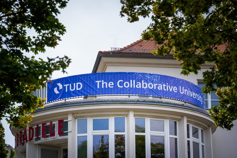 Photo: TUD information desk on Mommsenstraße with the lettering "Welcome". The Fritz-Foerster-Bau is reflected in the window.