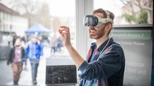 Foto: Person mit Virtual-Reality-Brille steht vor einem Fenster und gestikuliert mit der rechten Hand