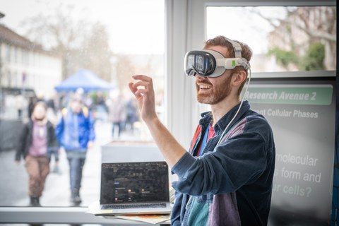 Foto: Person mit Virtual-Reality-Brille steht vor einem Fenster und gestikuliert mit der rechten Hand