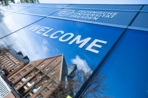 Foto: TUD-Information auf der Mommsenstraße mit dem Schriftzug "Welcome". In der Scheibe spiegelt sich der Fritz-Foerster-Bau.