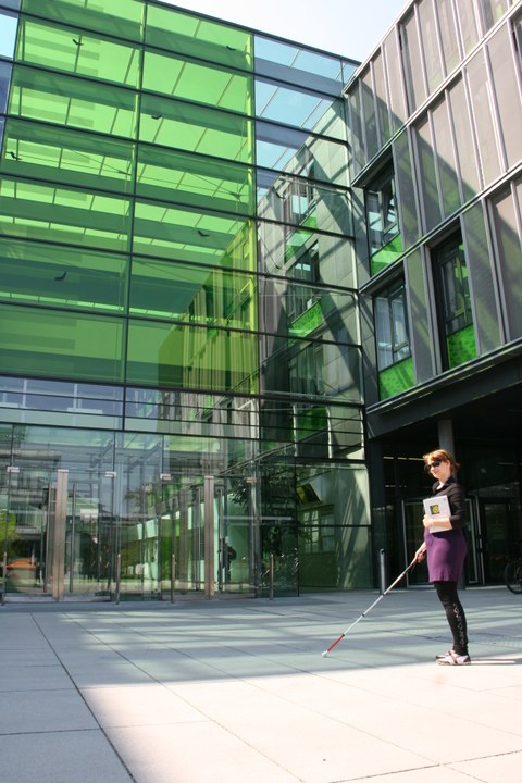 Photo of the entrance area of the Andreas-Pfitzmann Building by day. In the foreground is a woman with a cane for the blind.