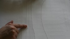 Foto eines taktilen Ausdrucks eines Kurvendiagramms. Zwei Hände ertasten die Linien der Grafik.