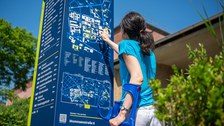 Foto einer Person mit Krücken, die versucht sich mit Hilfe einer Informationskarte auf dem TU Campus zu orientieren
