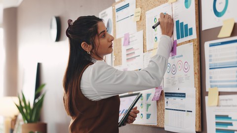 Photo of a person at a bulletin board with many notes displaying diagrams. 