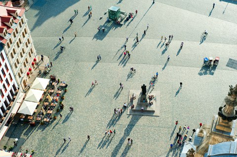 Das Foto zeigt Personen auf dem Dresdner Neumarkt. Es wurde aus der Vogelperspektive aufgenommen. In der Mitte des Platzes erkennt man eine Statue.