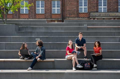 Bild zeigt 5 Studierende, die sich auf den Treppen am Fritz-Foerster-Bau unterhalten und zusammen lernen.