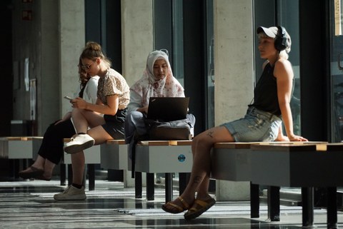 Fotos von vier Personen, die auf dem Campus der TU Dresden auf Bänke sitzend etwas anhören oder auf den Laptop oder das Handy schauen.
