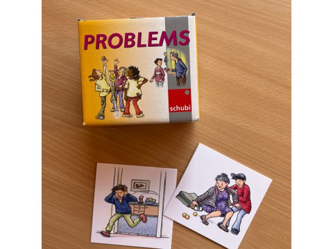 Auf dem Tisch liegt das Kartensetspiel "Problems" davor liegen zwei Karten aus dem Set als Anschauungsbeispiele.