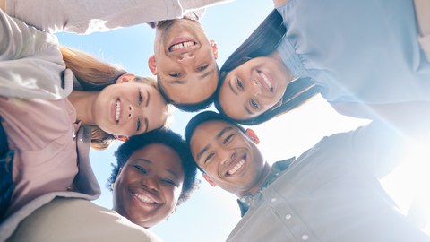 Eine Gruppe von diversen Menschen steht gemeinsam im Kreis und berät sich