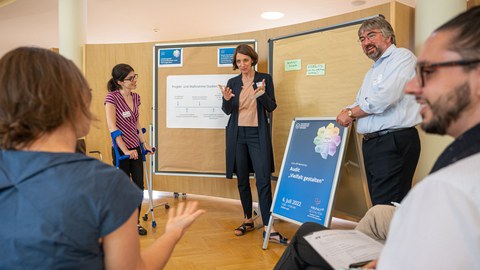 Professorin Böhm und Herr Prof. Ganseuer im Gespräch mit Workshopteilnehmenden. Im Hintergrund stehen Planwände zur Sicherung von Ideen und Ergebnissen.